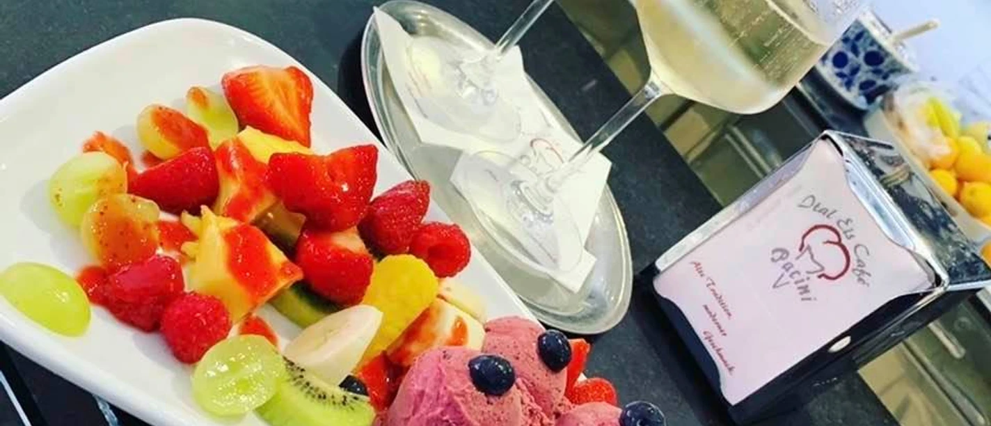 Eiscafé Pacini_Luebbecke.jpg Frisches Obst und drei Kugeln Fruchteis mit Gläsern Weißwein auf einem Tisch im Eiscafé.