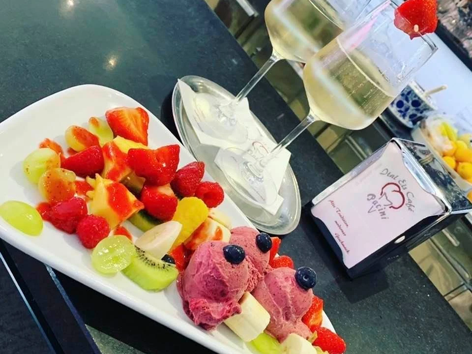 Eiscafé Pacini_Luebbecke.jpg Frisches Obst und drei Kugeln Fruchteis mit Gläsern Weißwein auf einem Tisch im Eiscafé.