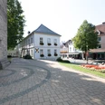 Pflastersteine vor der Kirche, mit Blumenbeet und historischen Gebäuden im Hintergrund.
