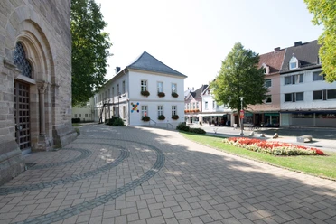 Kirchplatz und Fußgängerzone in Steinheim Pflastersteine vor der Kirche, mit Blumenbeet und historischen Gebäuden im Hintergrund.