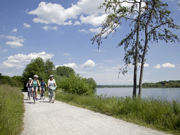 Radfahrer auf einem sonnigen Weg am Lippesee, flache Vegetation und blauer Himmel im Hintergrund.