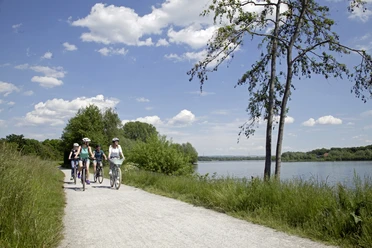 Radler am Lippesee Radfahrer auf einem sonnigen Weg am Lippesee, flache Vegetation und blauer Himmel im Hintergrund.