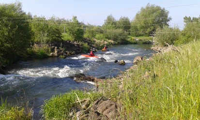 Kanuten auf der Lippe Zwei Kanuten manövrieren ihre Boote durch das sprudelnde Wasser eines Flusses, umgeben von grüner Natur.