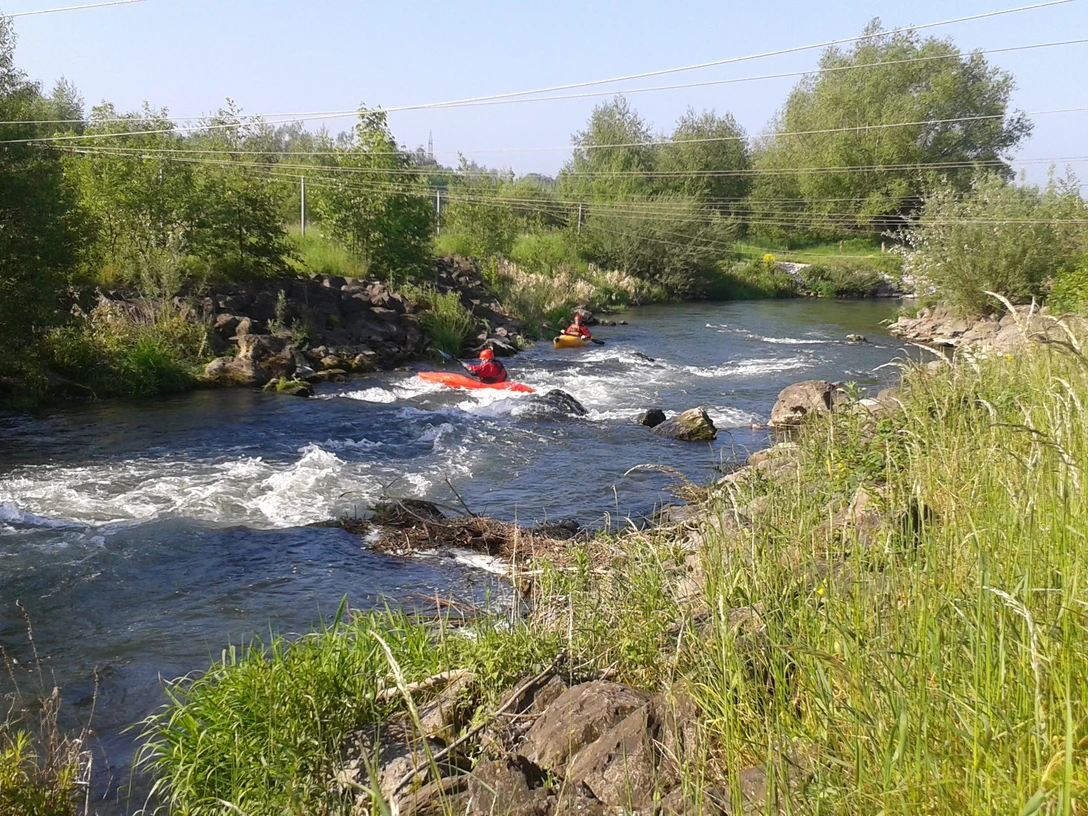 Kanuten auf der Lippe Zwei Kanuten manövrieren ihre Boote durch das sprudelnde Wasser eines Flusses, umgeben von grüner Natur.