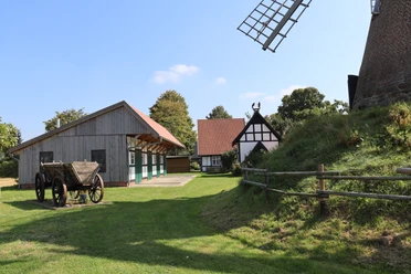 Windmühle Südhemmern Historische Windmühle mit Fachwerkhäusern und Holzwagen in ländlicher Umgebung unter blauem Himmel.