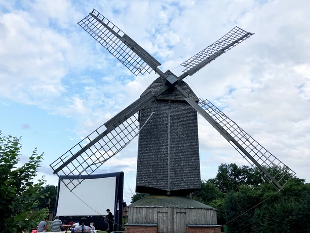 Bockwindmühle Wehe bei Bewölkung, Gruppenaktivitäten und Leinwand im Hintergrund sichtbar.