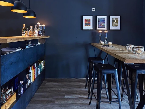 Lu´s Box Bistro.jpg Modern eingerichtete Bar mit industriellem Stil, dunklen Wänden, Holztresen und Hockern für Gäste.