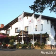 Gasthaus-Rose Gasthaus-Rose mit weißer Fassade und auffälligen Rosenaufhängungen, umgeben von hohen Fahnenmasten.