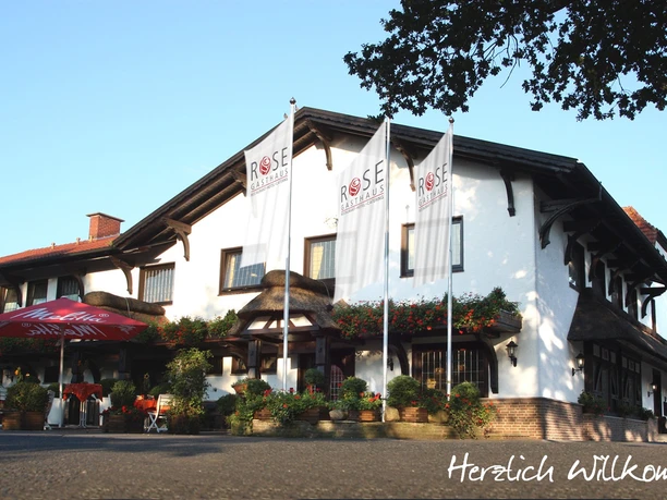 Gasthaus-Rose Gasthaus-Rose mit weißer Fassade und auffälligen Rosenaufhängungen, umgeben von hohen Fahnenmasten.