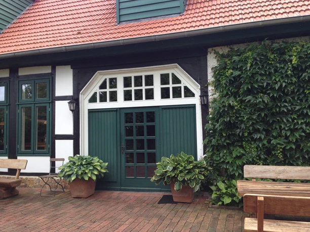 Gasthaus Schulenburg Fachwerkgebäude mit rotem Ziegeldach, Holzbänken, grüner Eingangstür und rankendem Efeu.