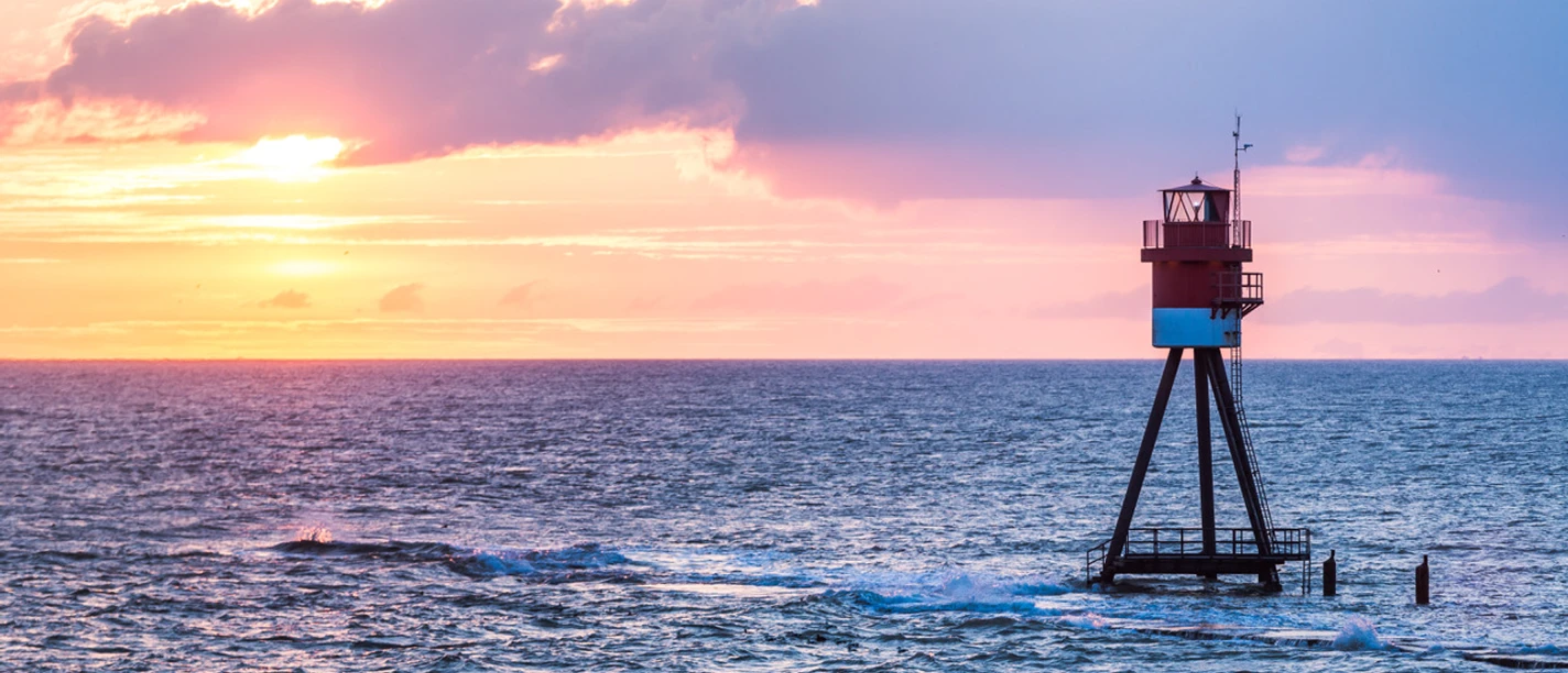 Fischerbalje Ein rot-weiß gestreifter Leuchtturm steht in der Weite des blauen Meeres bei Sonnenuntergang.