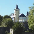 Schloss Homburg Gelbes Schloss mit Turm, umgeben von Bäumen, auf einem Hügel unter blauem Himmel.