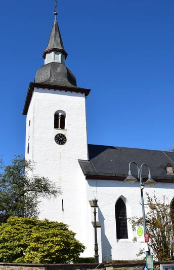 1000 jährige Kirche <p>Weiße Kirche mit Turm vor blauem Himmel, umgeben von blühenden Bäumen und Laterne.</p>