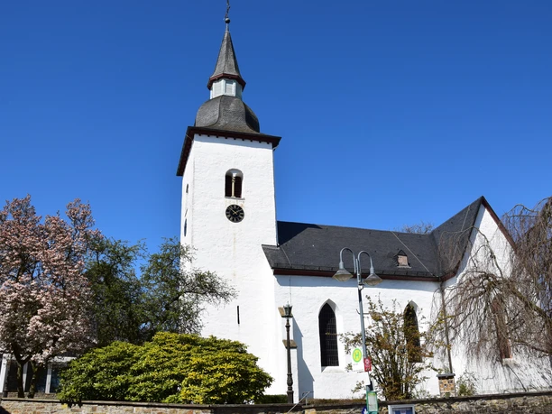 1000 jährige Kirche <p>Weiße Kirche mit Turm vor blauem Himmel, umgeben von blühenden Bäumen und Laterne.</p>