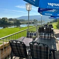 Die Terrasse des Restaurants bietet Tische und Stühle aus Metall, blaue Sonnenschirme und den Blick auf die Weser und Grünflächen.