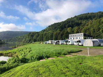 Camping am Bootshaus - Ansicht Blick auf Wohnwagenstellplatz, linksseitig die Weser, Bootshaus mit Terrasse und Bäumen im Hintergrund.