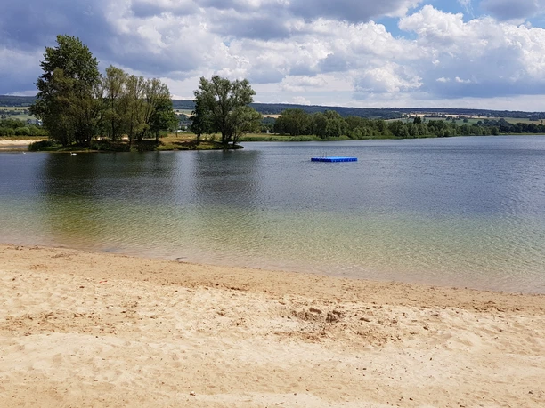 Badesee mit Sandstrand und Badeplattform im See