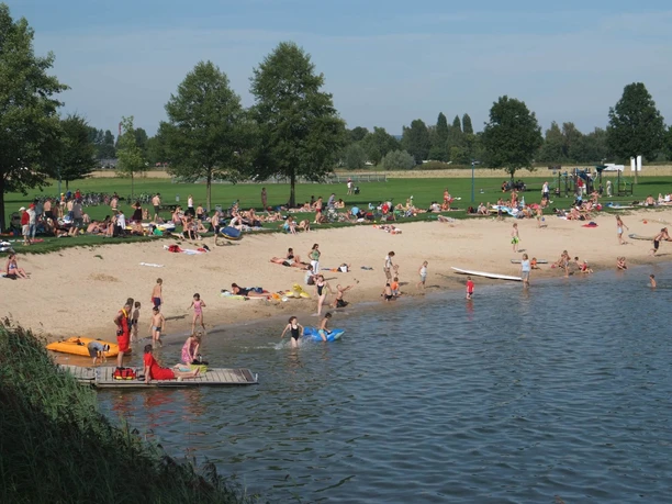 Menschen am Badestrand und im See, Liegewiese im Hintergrund