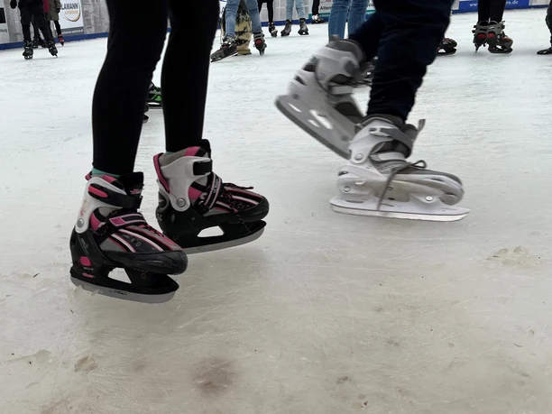 Schlittschuhläufer mit pinken und grauen Schlittschuhen gleiten über eine Eisbahn.