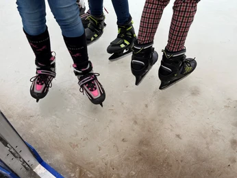 Schlittschuhe Drei Kinder mit bunten Schlittschuhen gleiten auf einer Eisfläche und erzeugen ein Gefühl von Winterspaß.
