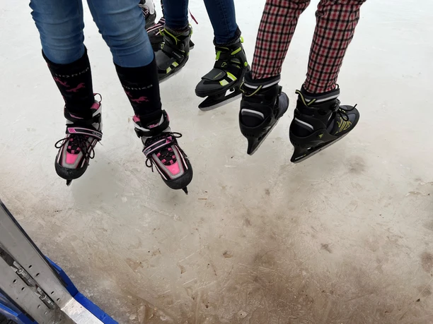 Schlittschuhe Drei Kinder mit bunten Schlittschuhen gleiten auf einer Eisfläche und erzeugen ein Gefühl von Winterspaß.