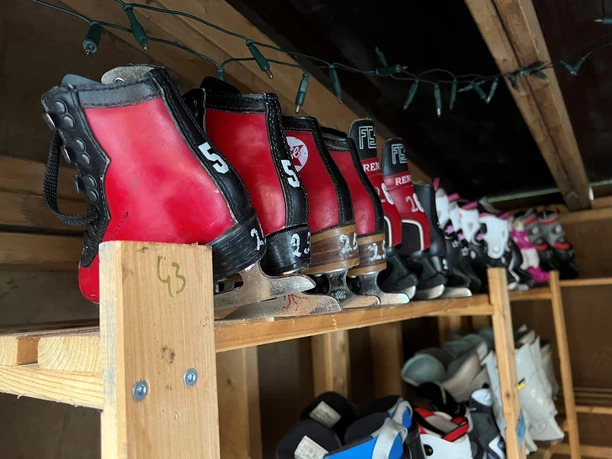 Various red and white skates are neatly stacked on a wooden shelf.
