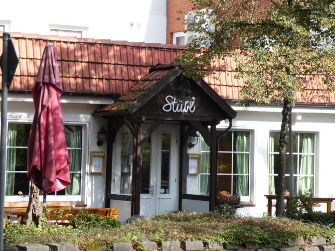 Eingang eines traditionellen Gebäudes mit Spitzdach, rotem Ziegeldach und grünen Fensterläden.