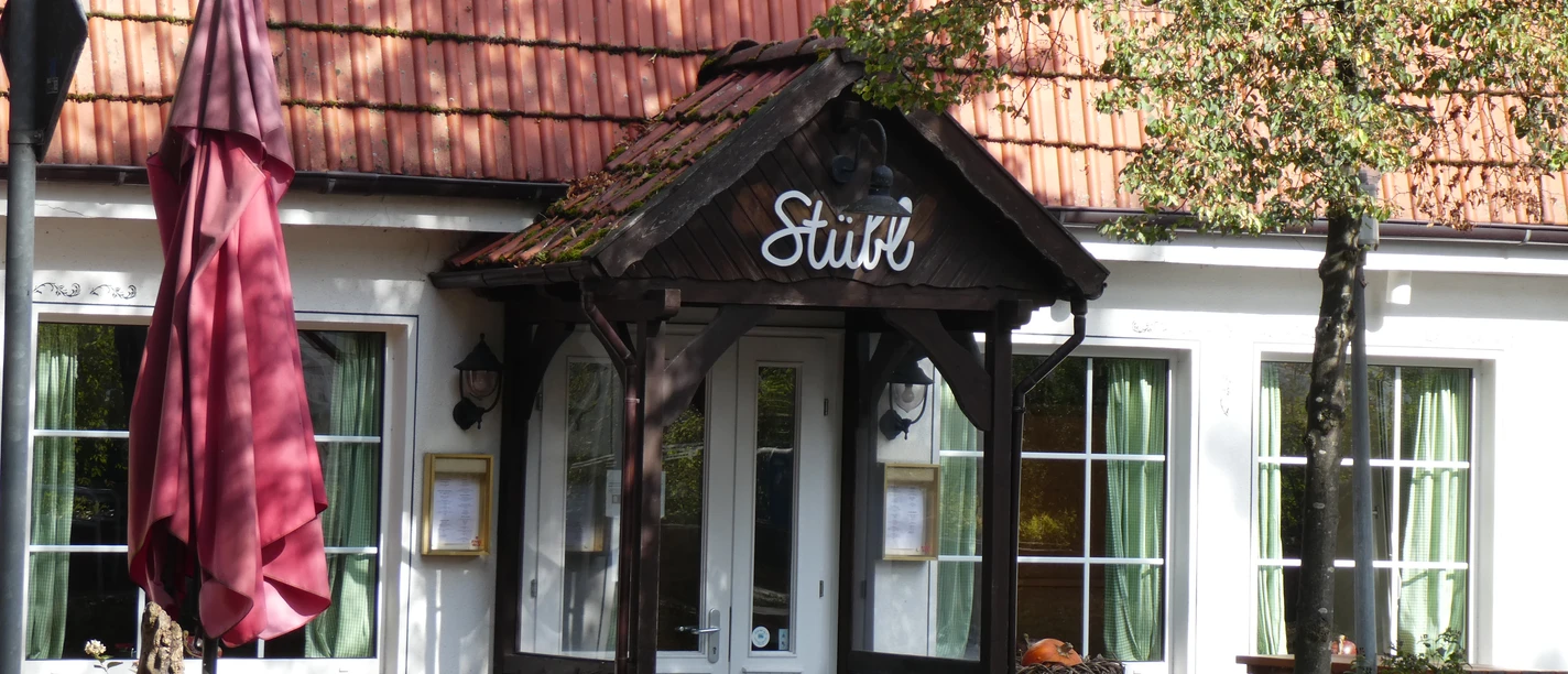 Landhaus Wesermarsch Eingang eines traditionellen Gebäudes mit Spitzdach, rotem Ziegeldach und grünen Fensterläden.