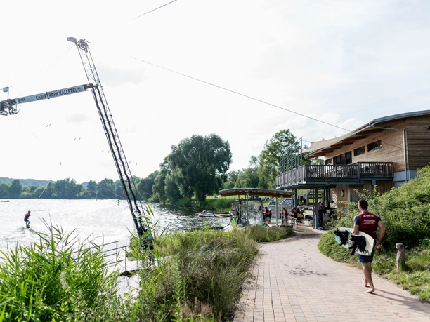 Campingpark Kalletal - Wasserski Person mit Board geht an der Wasserskianlage entlang