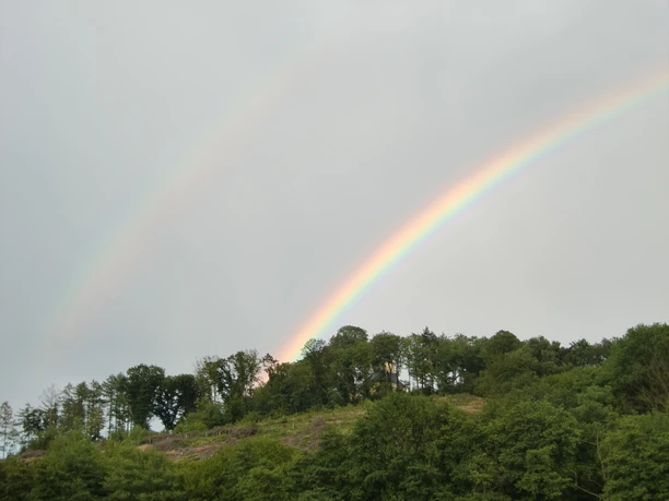 Regenbogen bei Huppichteroth Doppelte Regenbögen über bewaldetem Hügel, bei grauem Himmel mit sattem Grün im Vordergrund.