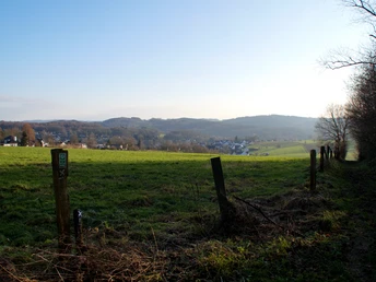 Haferspanienroute Grüne hügelige Landschaft bei Sonnenschein, mit Dörfern und Wäldern im Hintergrund.