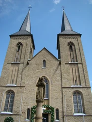 Marialindener Dom Die prächtige Kirche von Overath mit zwei markanten Türmen und einer Heiligenstatue im Vordergrund.
