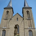 Marialindener Dom Die prächtige Kirche von Overath mit zwei markanten Türmen und einer Heiligenstatue im Vordergrund.