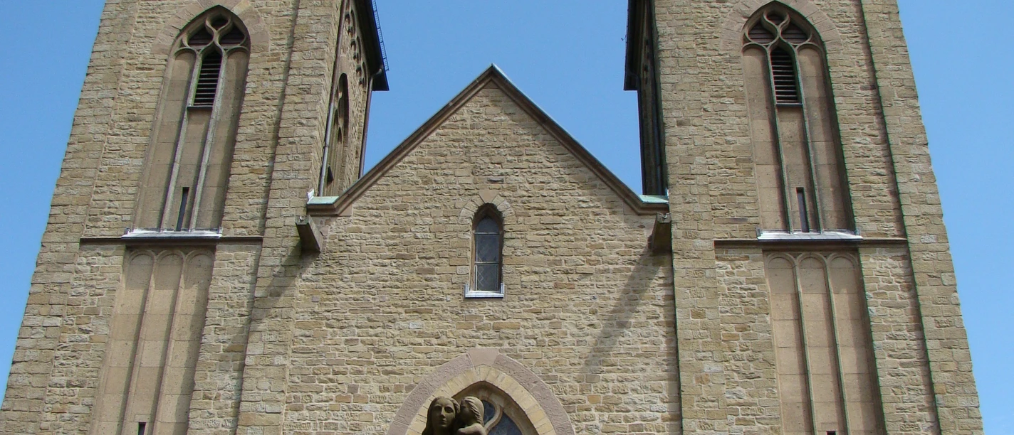 Marialindener Dom Die prächtige Kirche von Overath mit zwei markanten Türmen und einer Heiligenstatue im Vordergrund.