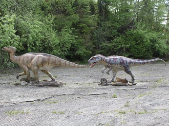 Dino-Park Zwei lebensgroße Dinosauriermodelle auf einer steinigen Fläche, umgeben von dichtem Grün.