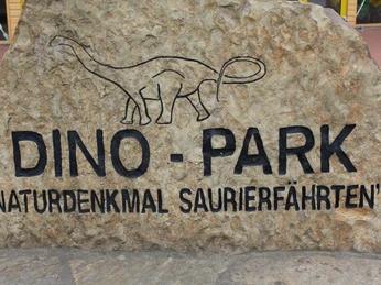 Massiver Steinblock mit eingraviertem Dinosaurier und Schriftzügen "Dino-Park" und "Naturdenkmal Saurierfährten".