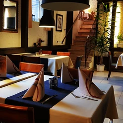 Gaststätte Fuchsbau_Luebbecke.jpg Geschmackvoll gedeckter Tisch in einem Restaurant mit gefaltetem Stoffservietten, vor einer Holztreppe.