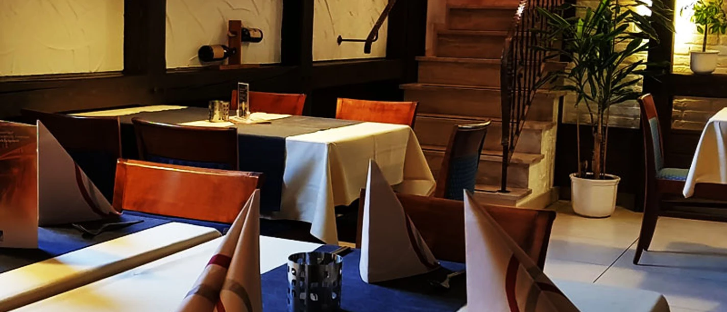 Gaststätte Fuchsbau_Luebbecke.jpg Geschmackvoll gedeckter Tisch in einem Restaurant mit gefaltetem Stoffservietten, vor einer Holztreppe.