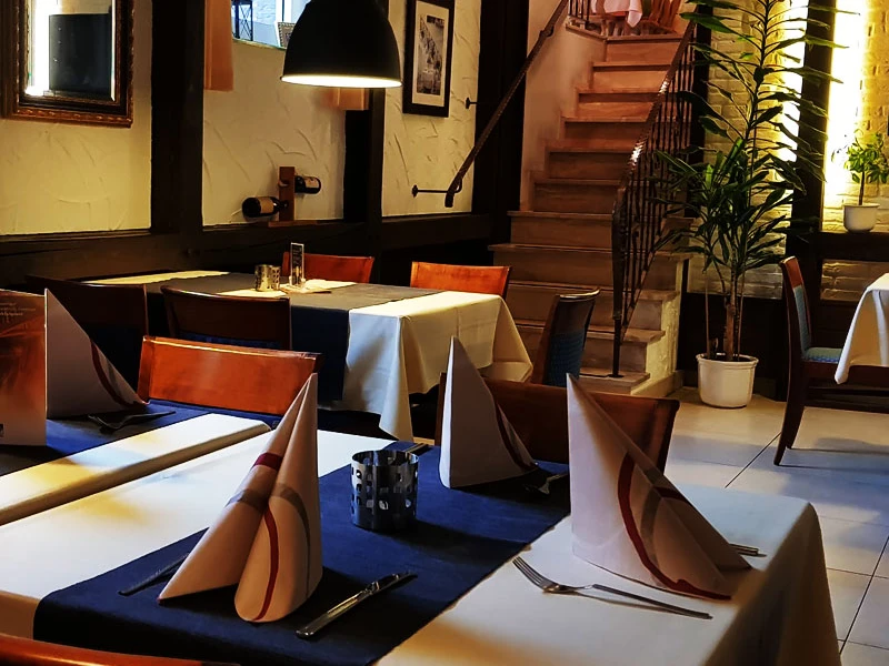 Gaststätte Fuchsbau_Luebbecke.jpg Geschmackvoll gedeckter Tisch in einem Restaurant mit gefaltetem Stoffservietten, vor einer Holztreppe.