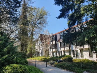 Holsing Vital Gesundheitszentrum in grüner Umgebung mit modernem Gebäude, umgeben von Bäumen und Sträuchern.