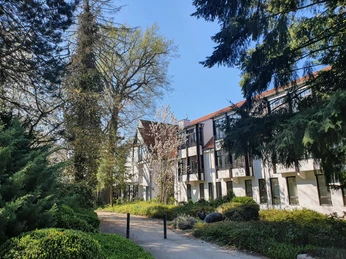 Holsing Vital Gesundheitszentrum in grüner Umgebung mit modernem Gebäude, umgeben von Bäumen und Sträuchern.