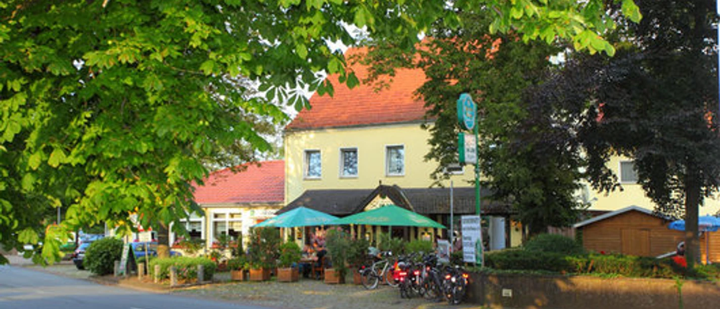 Hotel und Restaurant im Loh Espelkamp.jpg Hotel und Restaurant mit bunten Sonnenschirmen, umgeben von Bäumen, liegt an einer ruhigen Straße.