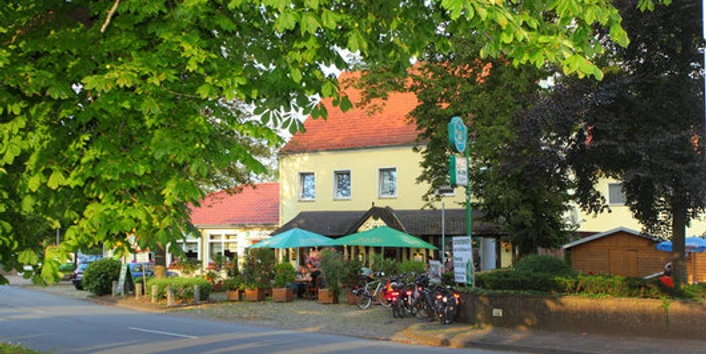 Hotel und Restaurant im Loh Espelkamp.jpg Hotel und Restaurant mit bunten Sonnenschirmen, umgeben von Bäumen, liegt an einer ruhigen Straße.