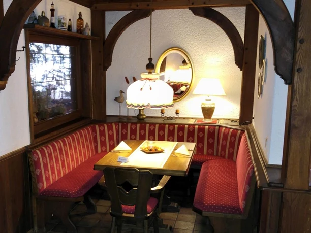 Eine gemütliche Sitzecke im Hotel-Restaurant Lindenhof mit roter Polsterbank und hölzernem Tisch.