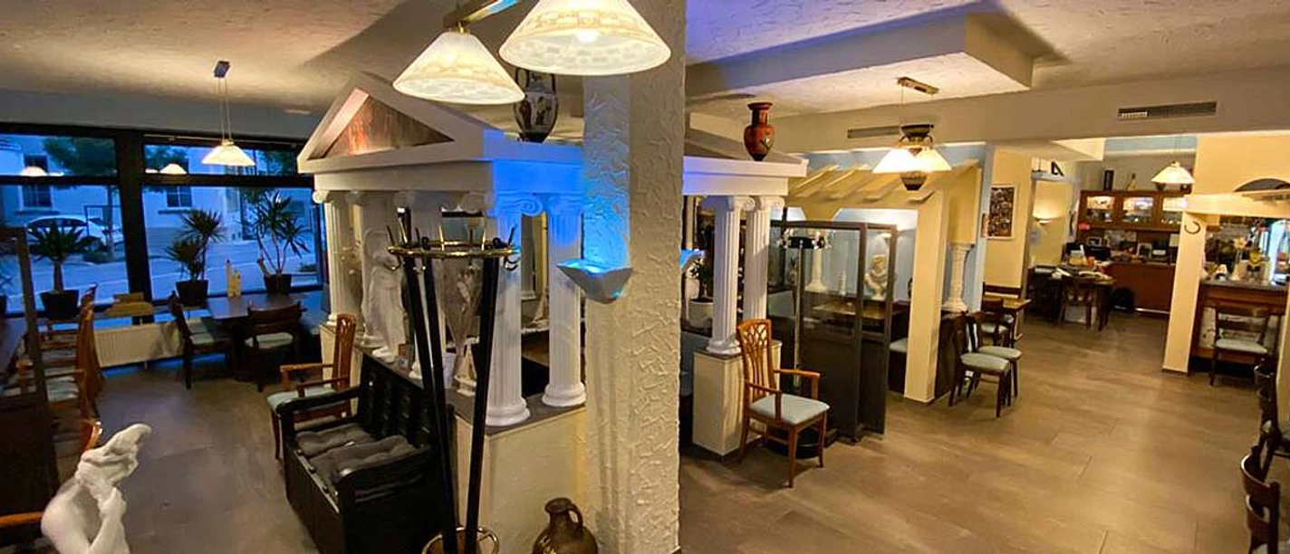 Ilias Taverne_Luebbecke.jpg Innenraum einer griechischen Taverne mit Säulen, warmem Licht und traditionellen Dekorationen.