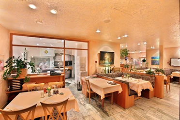 Italia Da Silvio_luebbecke.png Ein italienisches Restaurant mit warmem Ambiente, Holzmöbeln und gedeckten Tischen, im Hintergrund eine Küche.