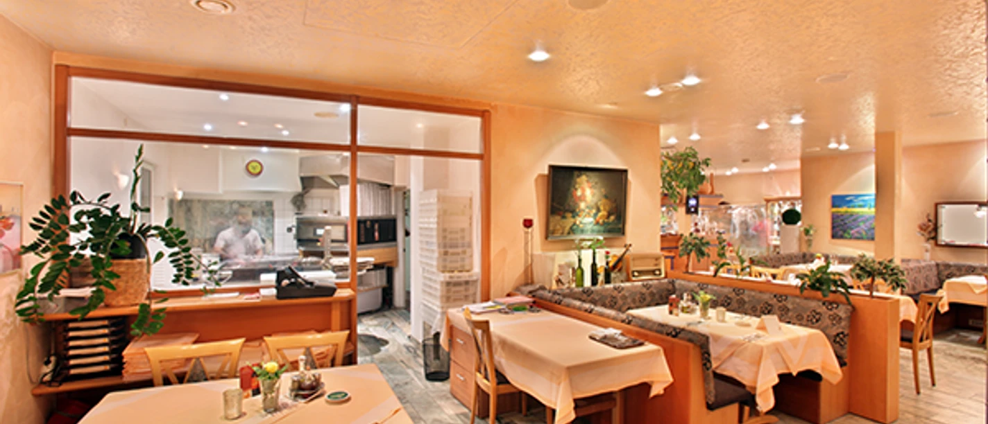 Italia Da Silvio_luebbecke.png Ein italienisches Restaurant mit warmem Ambiente, Holzmöbeln und gedeckten Tischen, im Hintergrund eine Küche.