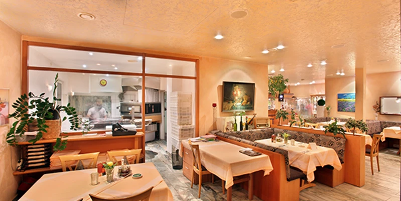 Italia Da Silvio_luebbecke.png Ein italienisches Restaurant mit warmem Ambiente, Holzmöbeln und gedeckten Tischen, im Hintergrund eine Küche.