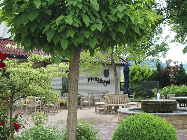 Kurhaus Pivittskrug Sonnige Terrasse des Kurhauses Pivittskrug mit runden Holztischen und üppiger Grünbepflanzung.