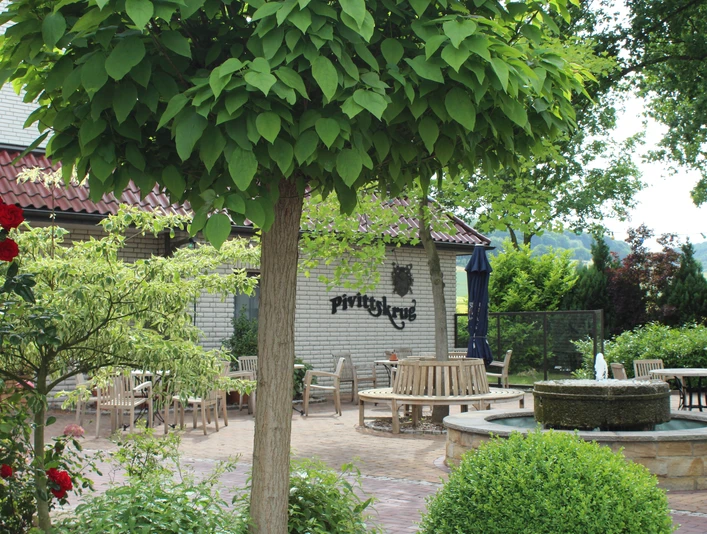 Kurhaus Pivittskrug Sonnige Terrasse des Kurhauses Pivittskrug mit runden Holztischen und üppiger Grünbepflanzung.